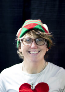 Carman Wellness Connections volunteer smiling while wearing a festive elf hat at a holiday community event.
