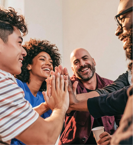 Four smiling adults bring their hands together in a group high-five, celebrating teamwork and connection.