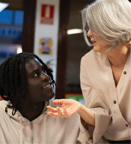 An older woman gestures while speaking with a younger man, sharing guidance during a one-on-one conversation.