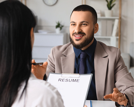 A man gestures while discussing a resumé with a woman during a job interview or career counselling session.