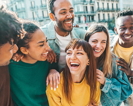 A diverse group of friends smile and laugh together outdoors, enjoying a moment of friendship and connection.